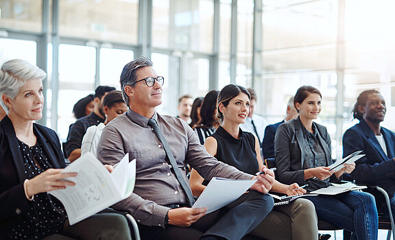 Das Publikum einer Konferenz macht sich Notizen zum Vortrag.